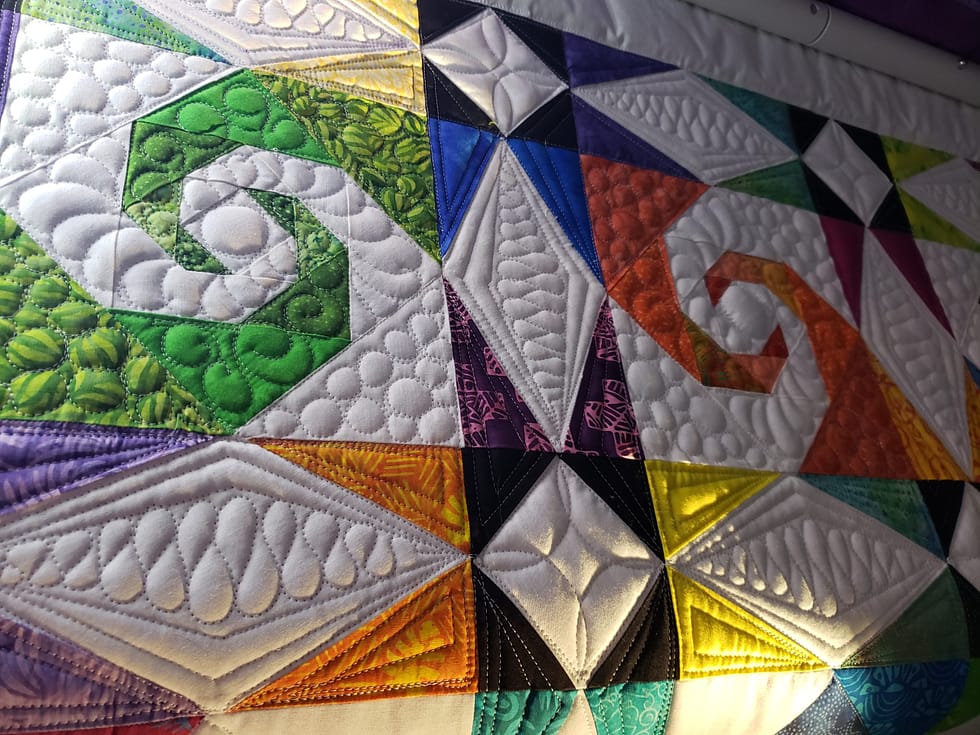 Quilts For Sale/ Quilt for Sale/ Quilt for Sale Handmade handmade quilts for sale/ Folded multi-color handmade Storm At Sea quilt on a chair, showing vibrant cotton fabrics and quilt stitching